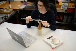 Molly measuring a bottle at an indoor desk