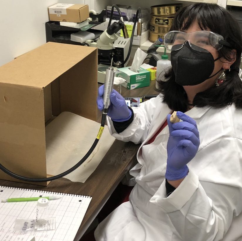 Andrea Levinson, recipient of the 2022 Sherri Gust Memorial Scholarship, wearing goggles and a white lab coat in the archeology lab.
