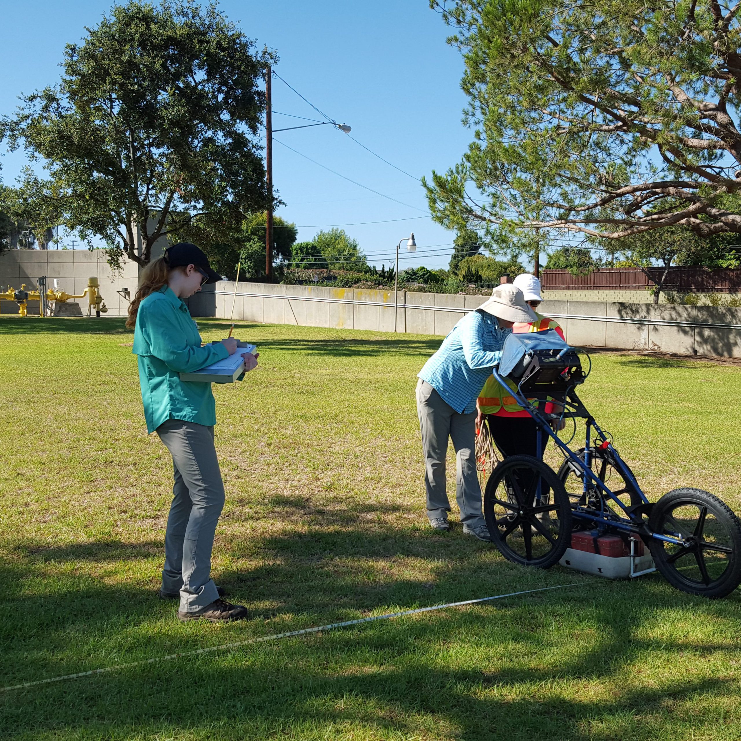 Three technicians using a ground-penetrating radar mounted on three wheels.
