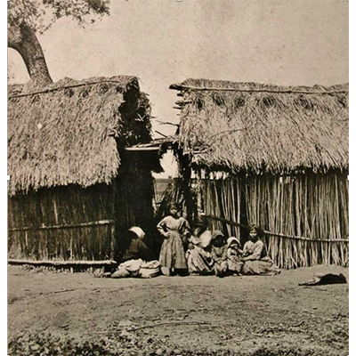 A black and white photo of a family outside of a hut